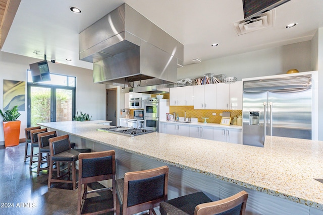 kitchen with light stone counters, wall chimney exhaust hood, stainless steel appliances, white cabinets, and decorative backsplash
