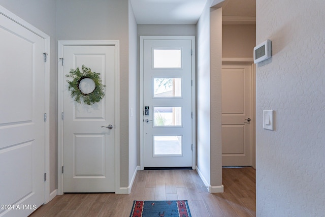 foyer featuring baseboards, light wood-style floors, and a textured wall