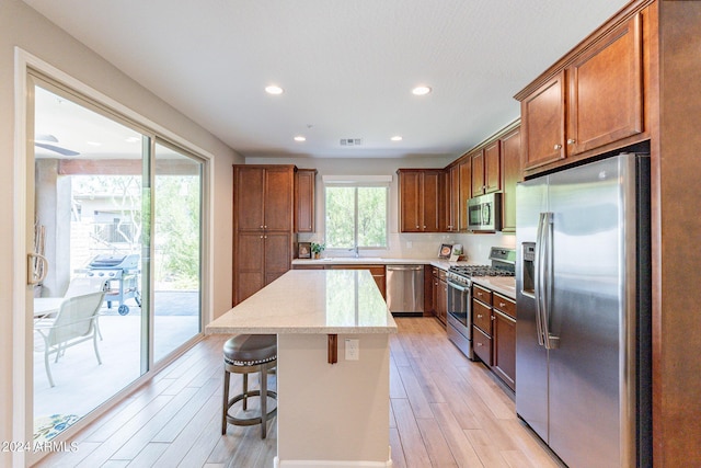 kitchen with brown cabinetry, light wood-style flooring, a center island, and appliances with stainless steel finishes