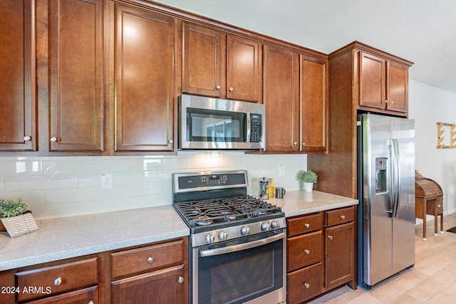 kitchen with brown cabinetry, stainless steel appliances, backsplash, and light stone countertops