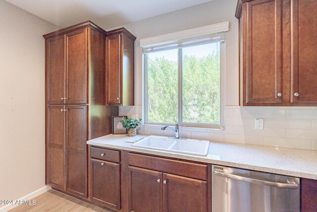 kitchen featuring light countertops, a sink, backsplash, dishwasher, and light wood-style floors