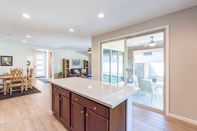 kitchen with ceiling fan, light stone counters, dark brown cabinetry, and light wood-type flooring