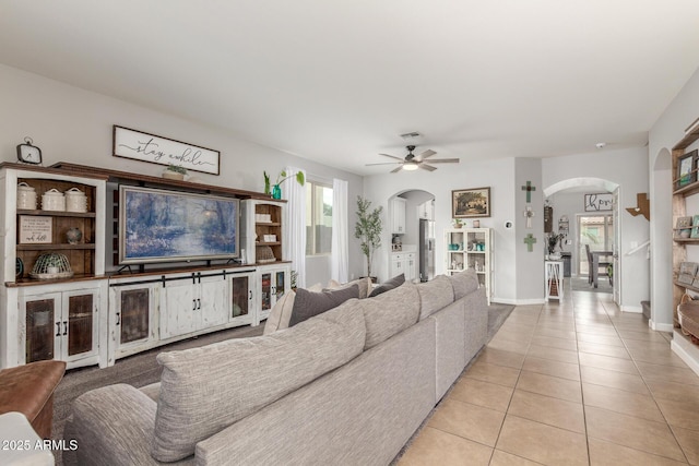 living area with ceiling fan, baseboards, arched walkways, and light tile patterned flooring