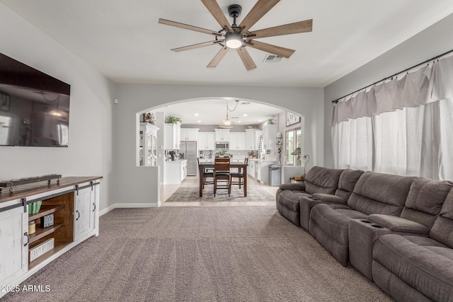 living room featuring baseboards, visible vents, arched walkways, ceiling fan, and light carpet