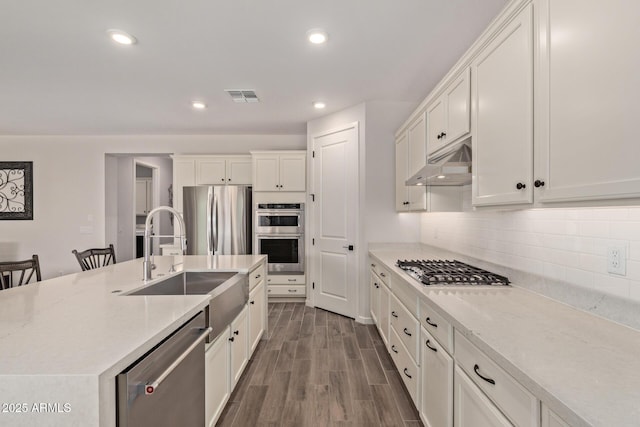 kitchen featuring under cabinet range hood, stainless steel appliances, a sink, visible vents, and dark wood finished floors