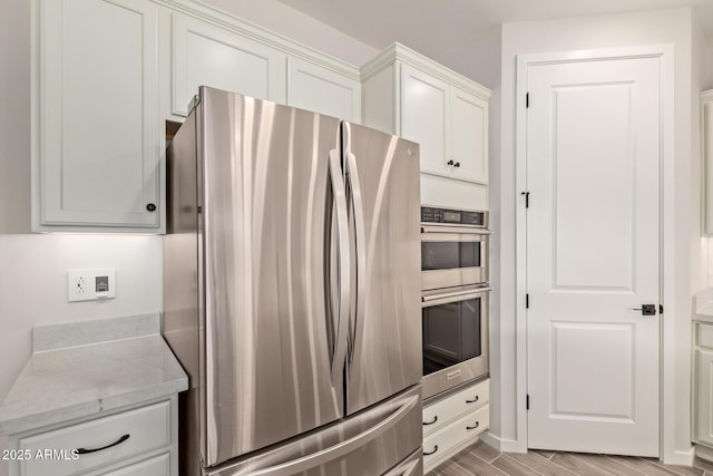 kitchen with light wood finished floors, white cabinetry, appliances with stainless steel finishes, and light stone counters