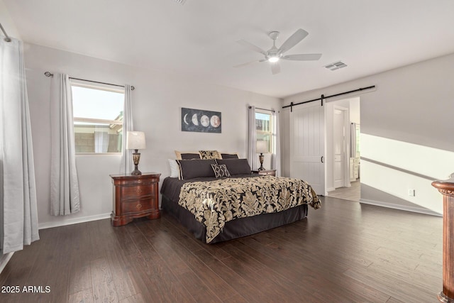 bedroom with a barn door, multiple windows, visible vents, and wood finished floors