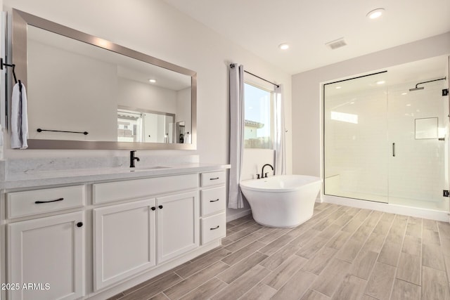 full bath with visible vents, vanity, a freestanding tub, a shower stall, and wood finish floors