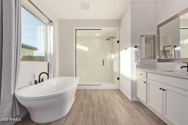 bathroom with a stall shower, wood finish floors, a freestanding tub, and vanity