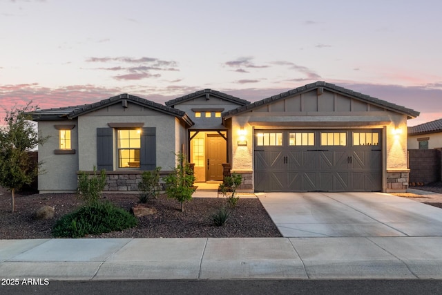 view of front of house featuring a tile roof, stucco siding, concrete driveway, an attached garage, and stone siding