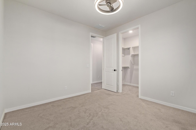 unfurnished bedroom with carpet, a walk in closet, visible vents, and baseboards