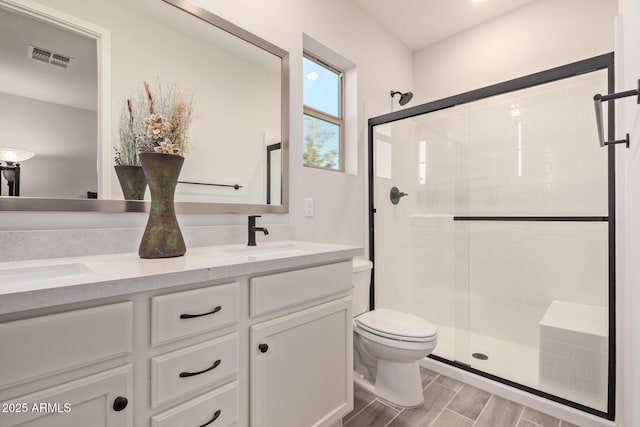 bathroom with a stall shower, a sink, toilet, and double vanity