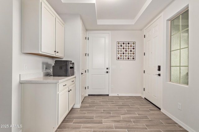 interior space with baseboards, white cabinets, a raised ceiling, wood tiled floor, and light countertops