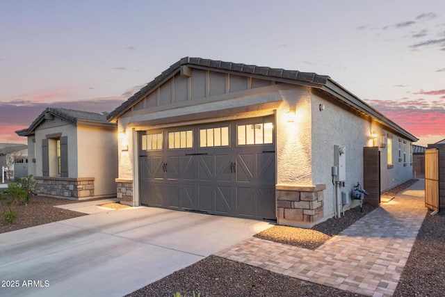 exterior space with stone siding, an attached garage, a tiled roof, and stucco siding