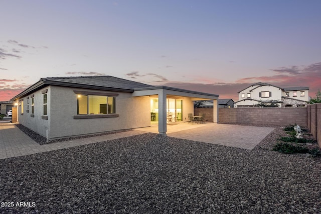 back of house at dusk featuring a tiled roof, a patio area, a fenced backyard, and stucco siding