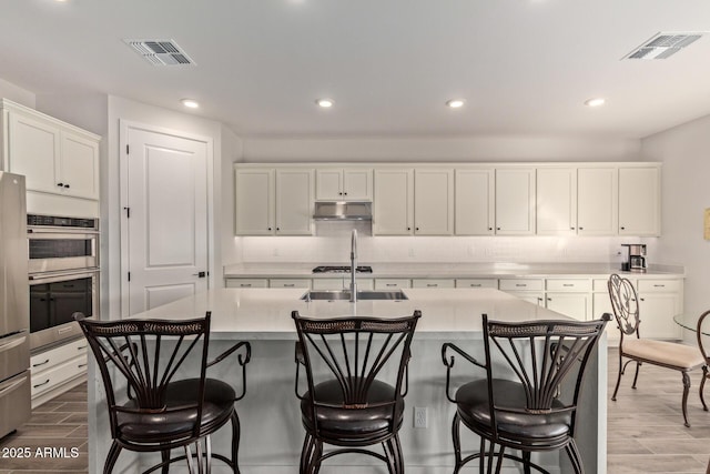 kitchen with under cabinet range hood, white cabinetry, visible vents, and light countertops