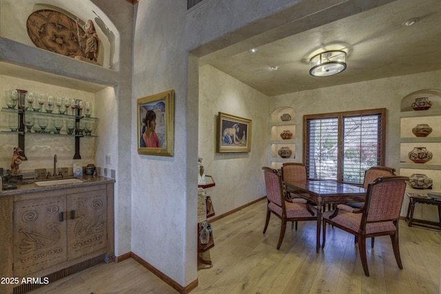 dining area with light wood-type flooring, baseboards, and indoor wet bar