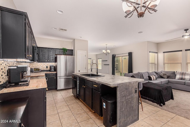 kitchen with light tile patterned flooring, sink, a center island with sink, stainless steel fridge, and black dishwasher