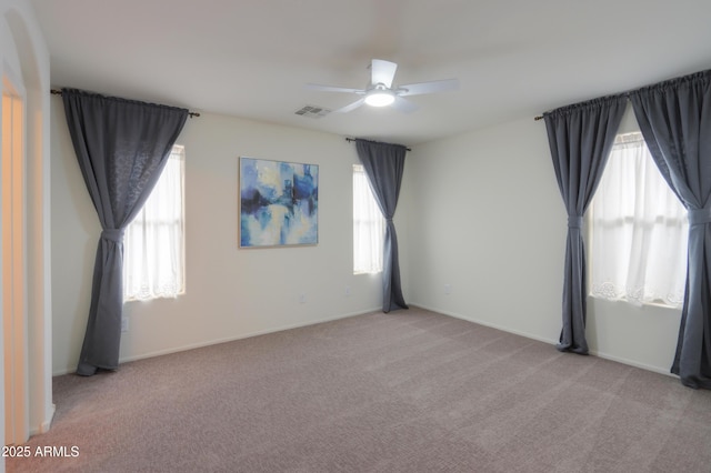 empty room featuring a ceiling fan, light carpet, visible vents, and baseboards