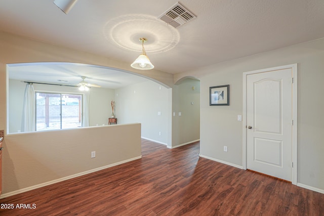 unfurnished room featuring arched walkways, visible vents, baseboards, and wood finished floors