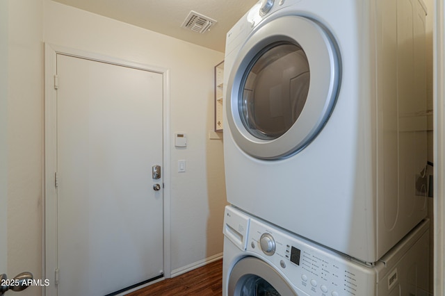 clothes washing area featuring laundry area, stacked washer and dryer, visible vents, baseboards, and dark wood finished floors