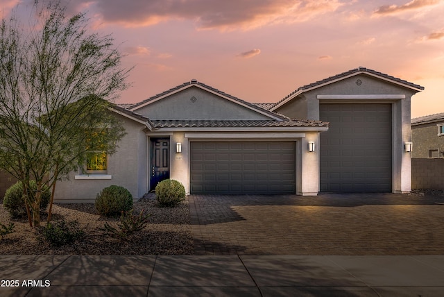 view of front of property featuring a tile roof, decorative driveway, an attached garage, and stucco siding