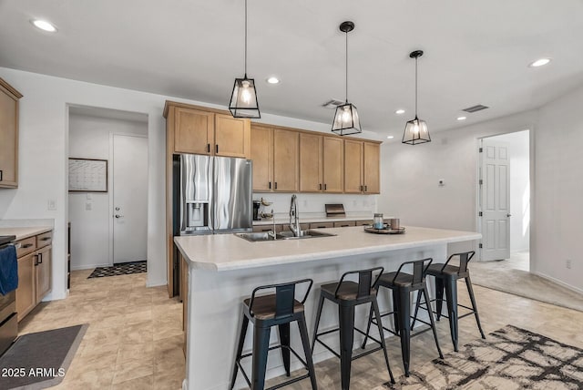 kitchen featuring recessed lighting, a sink, light countertops, stainless steel refrigerator with ice dispenser, and a kitchen bar