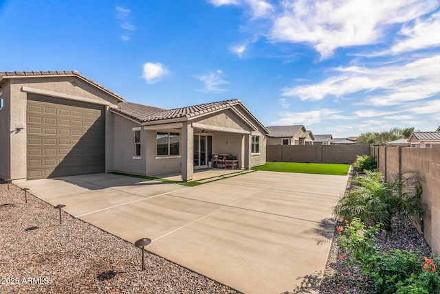 rear view of house featuring ceiling fan, a tiled roof, concrete driveway, stucco siding, and a fenced backyard