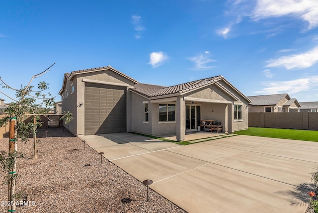 back of property featuring a tiled roof, concrete driveway, stucco siding, a fenced backyard, and an attached garage