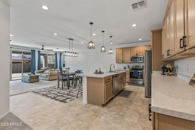 kitchen with a kitchen bar, a sink, open floor plan, appliances with stainless steel finishes, and light countertops