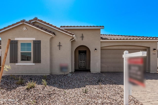 mediterranean / spanish-style home featuring stucco siding, an attached garage, a tile roof, and decorative driveway