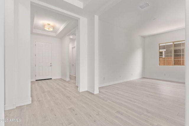unfurnished room with a tray ceiling, baseboards, light wood finished floors, and visible vents