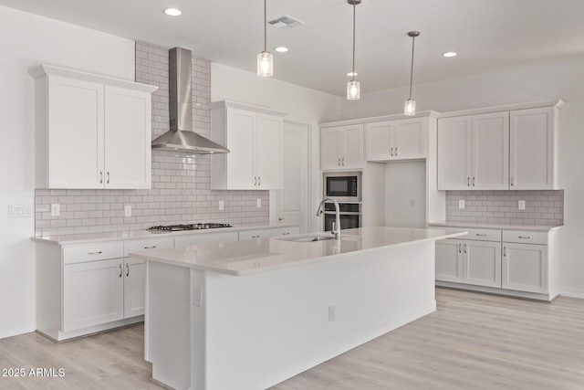 kitchen with white cabinets, visible vents, wall chimney exhaust hood, appliances with stainless steel finishes, and a sink