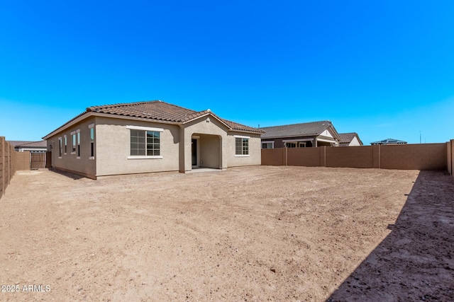 back of house featuring a fenced backyard, stucco siding, and a tiled roof