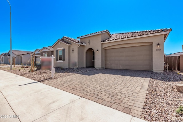 mediterranean / spanish home featuring stucco siding, fence, a tiled roof, decorative driveway, and a garage