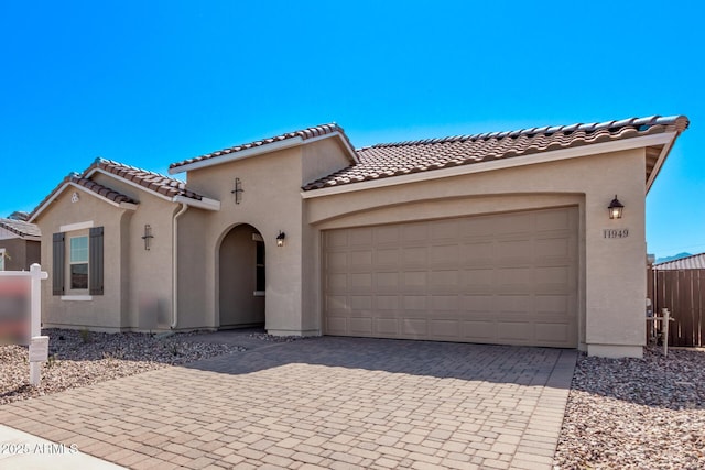 mediterranean / spanish-style home featuring stucco siding, an attached garage, a tiled roof, and decorative driveway