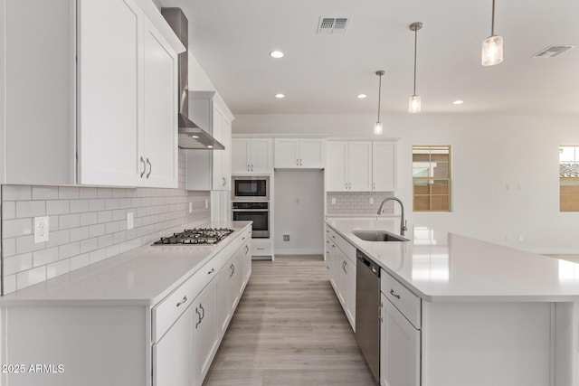 kitchen with white cabinets, visible vents, appliances with stainless steel finishes, a sink, and wall chimney range hood