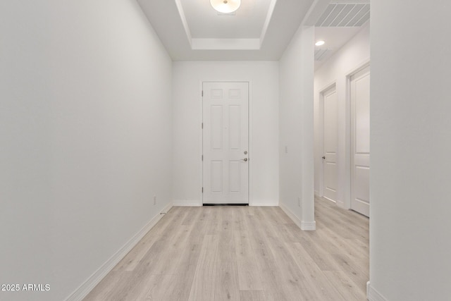 interior space with light wood finished floors, baseboards, visible vents, and a raised ceiling