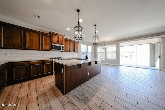 10036 E Naranja Ave, Mesa, AZ 85209 - kitchen featuring appliances with stainless steel finishes, a chandelier, a breakfast bar, wood tiled floors, and light stone countertops