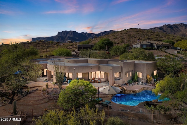 rear view of property featuring stucco siding, a mountain view, a patio area, and an outdoor pool