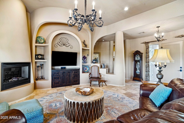 living area featuring a chandelier, built in features, a large fireplace, baseboards, and arched walkways