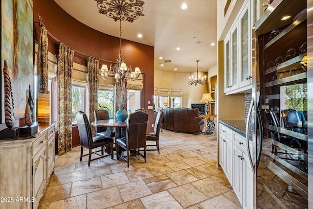dining area with a chandelier, recessed lighting, stone tile flooring, plenty of natural light, and a high ceiling