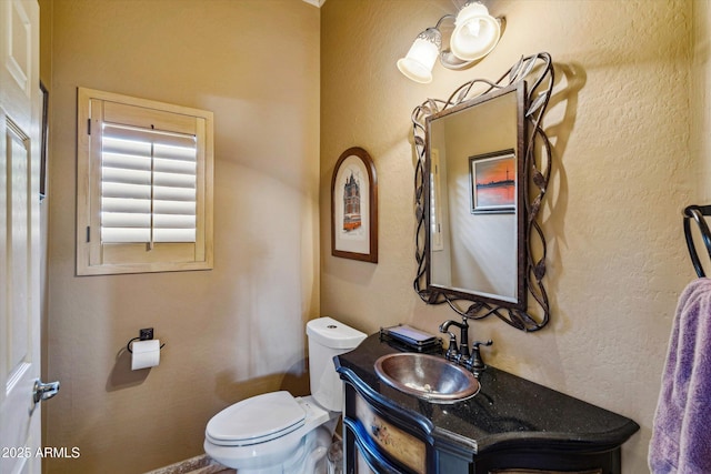 bathroom featuring toilet, vanity, and a textured wall