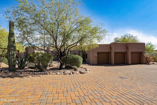 pueblo-style home with an attached garage, driveway, and stucco siding