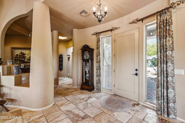 foyer entrance with stone tile flooring, arched walkways, a chandelier, and baseboards