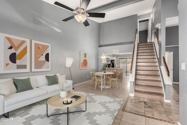 living room featuring ceiling fan, a high ceiling, stairway, and baseboards