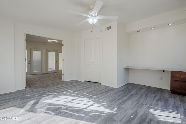 empty room with visible vents, a ceiling fan, wood finished floors, baseboards, and built in study area