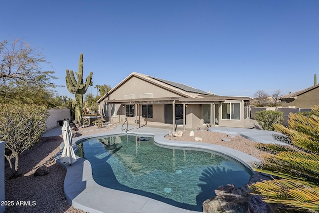 rear view of house with stucco siding, a patio, solar panels, and a fenced backyard