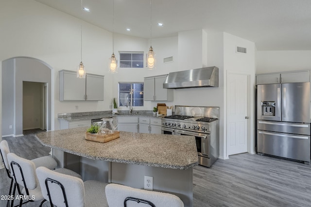 kitchen with stainless steel appliances, wall chimney range hood, high vaulted ceiling, gray cabinets, and a kitchen island