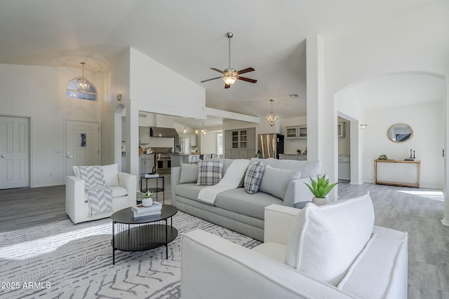 living room with light wood-style floors, arched walkways, high vaulted ceiling, and ceiling fan with notable chandelier